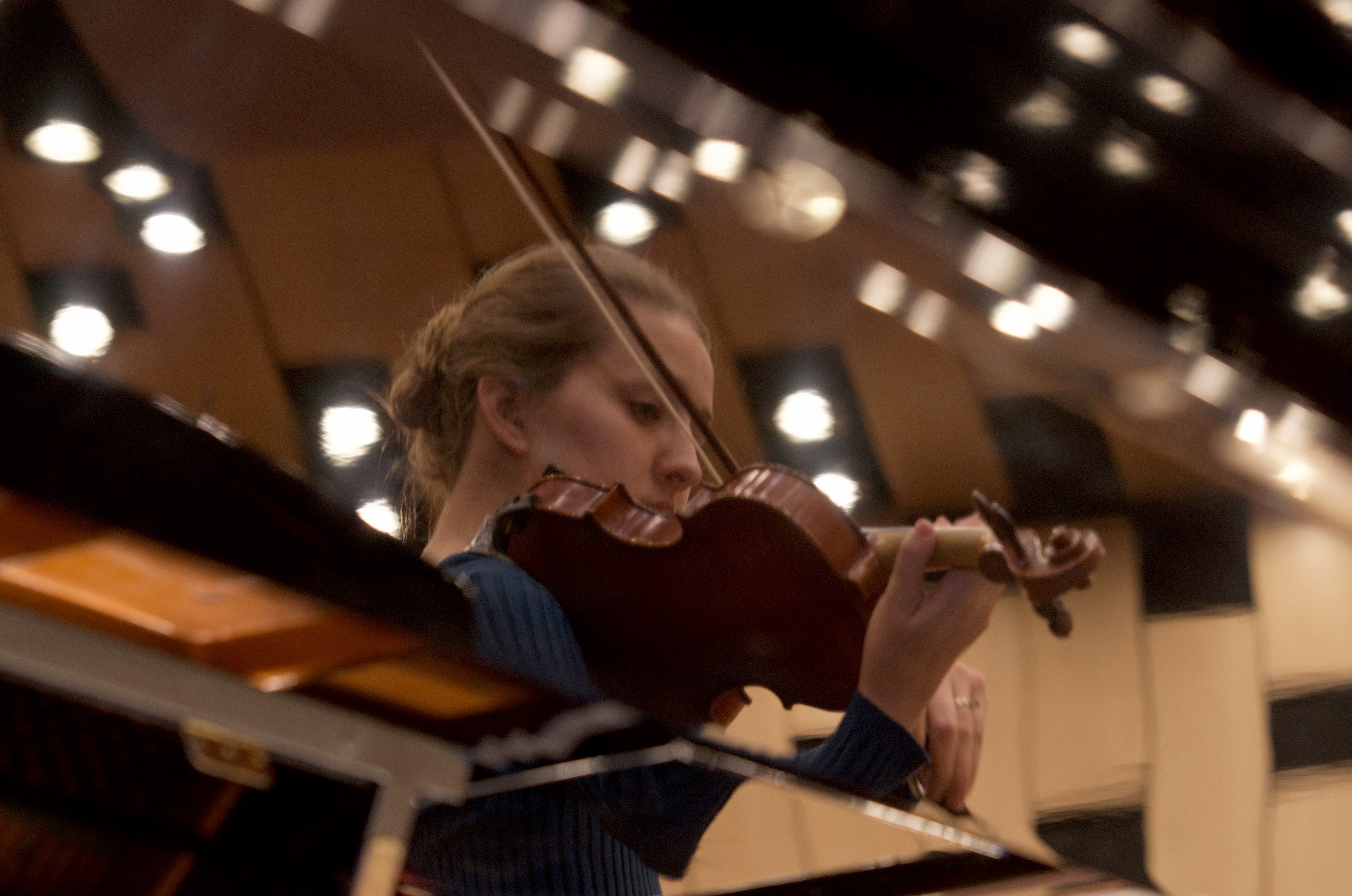 The reflection of a violinist performing, reflected off of the lid of a grand piano.