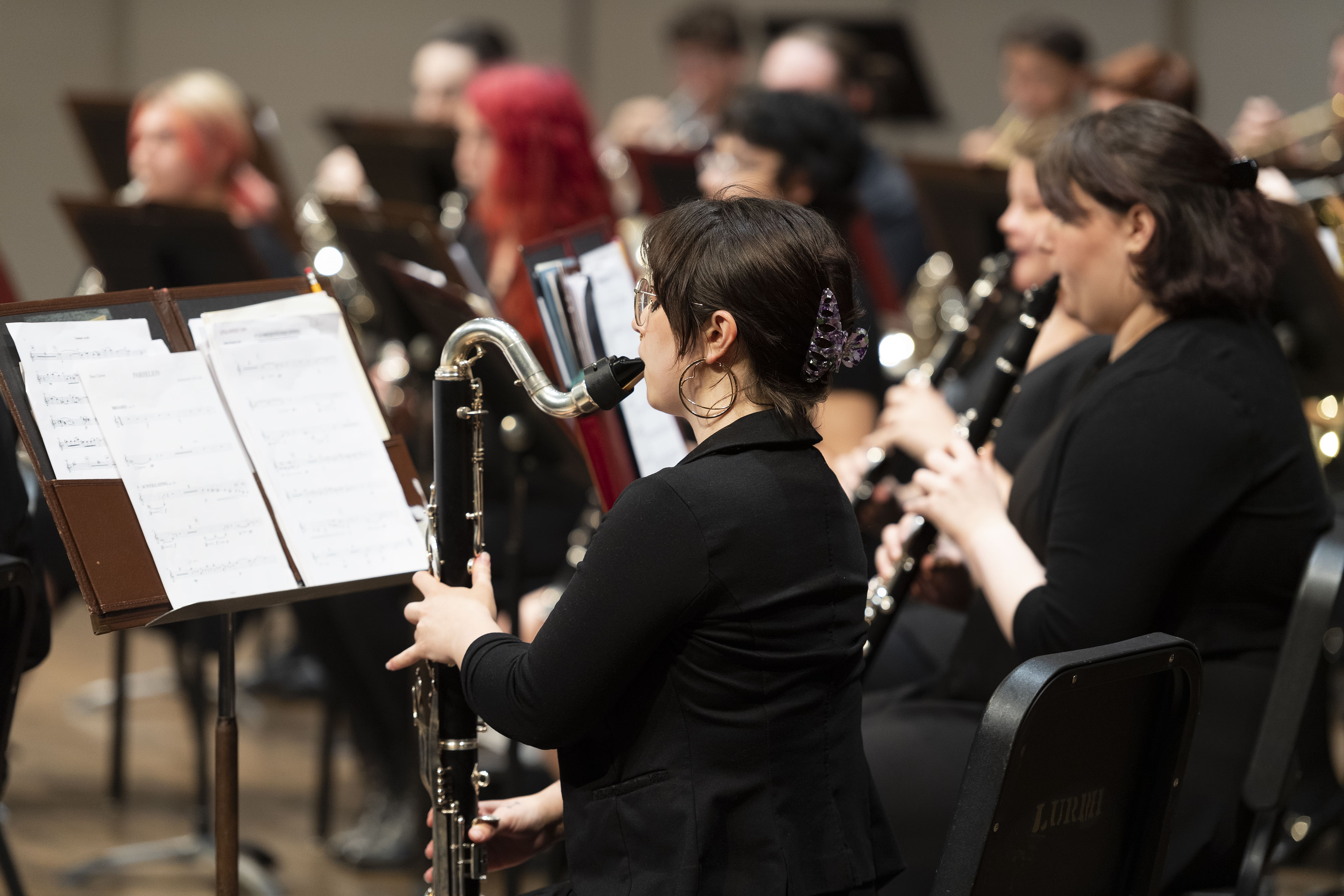 An over the shoulder shot of a bass clarinet player, with an out of focus band behind them.
