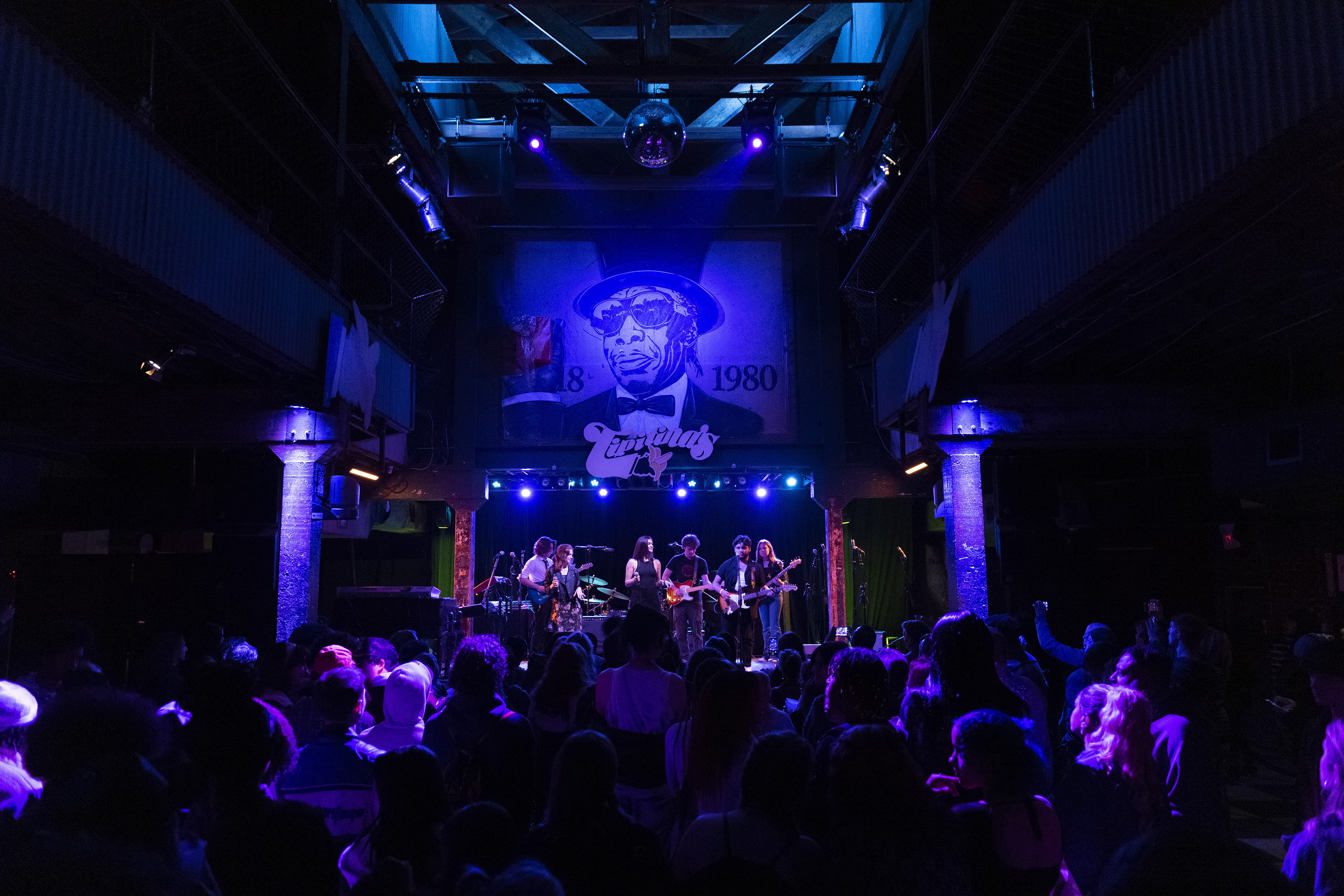 A full view of the Tipitina's concert venue, lit by soft blue light, with a Loyola band performing on stage.