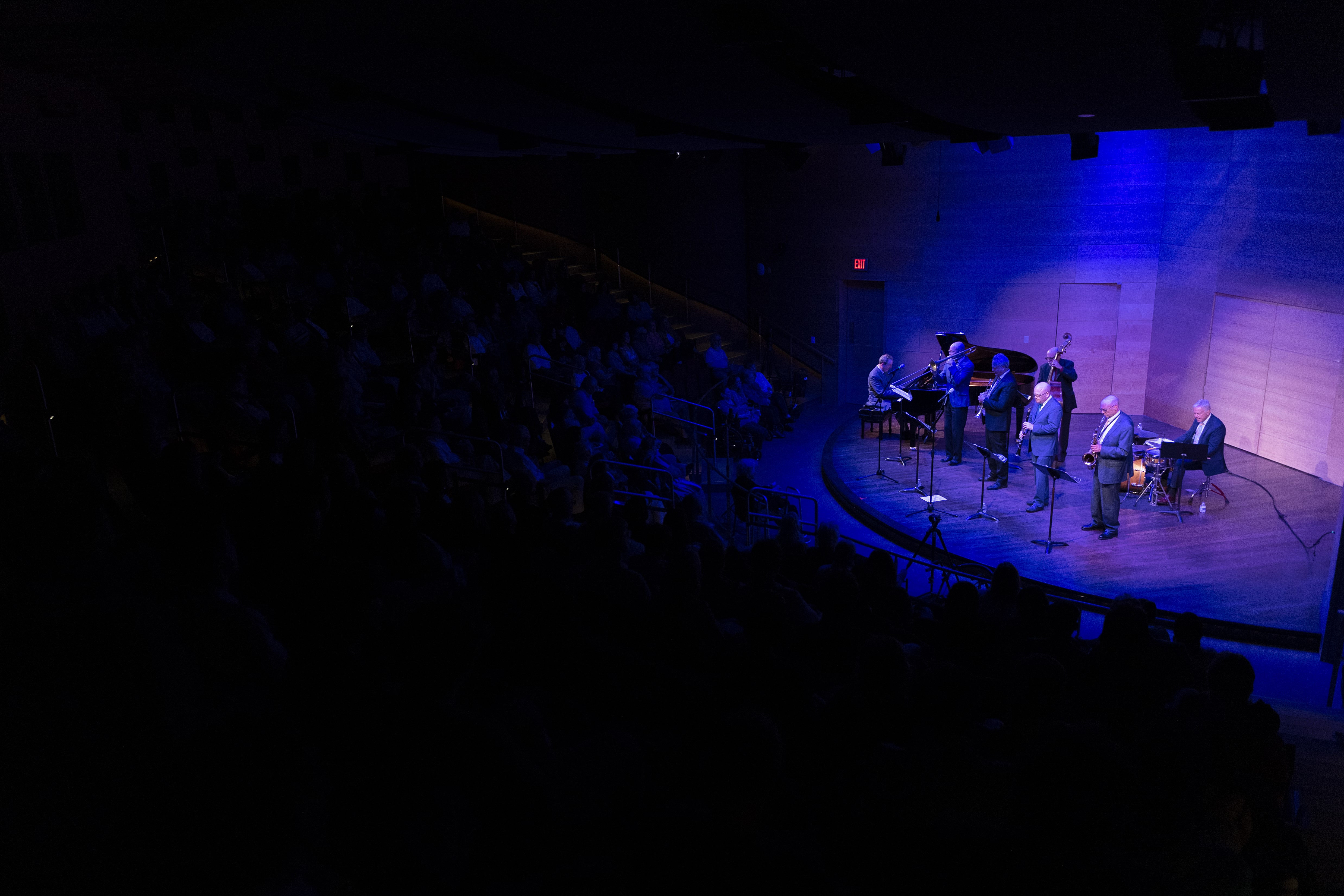 A packed Nunemaker Auditorium sits in darkness, listening to a jazz band on stage lit in soft blues.