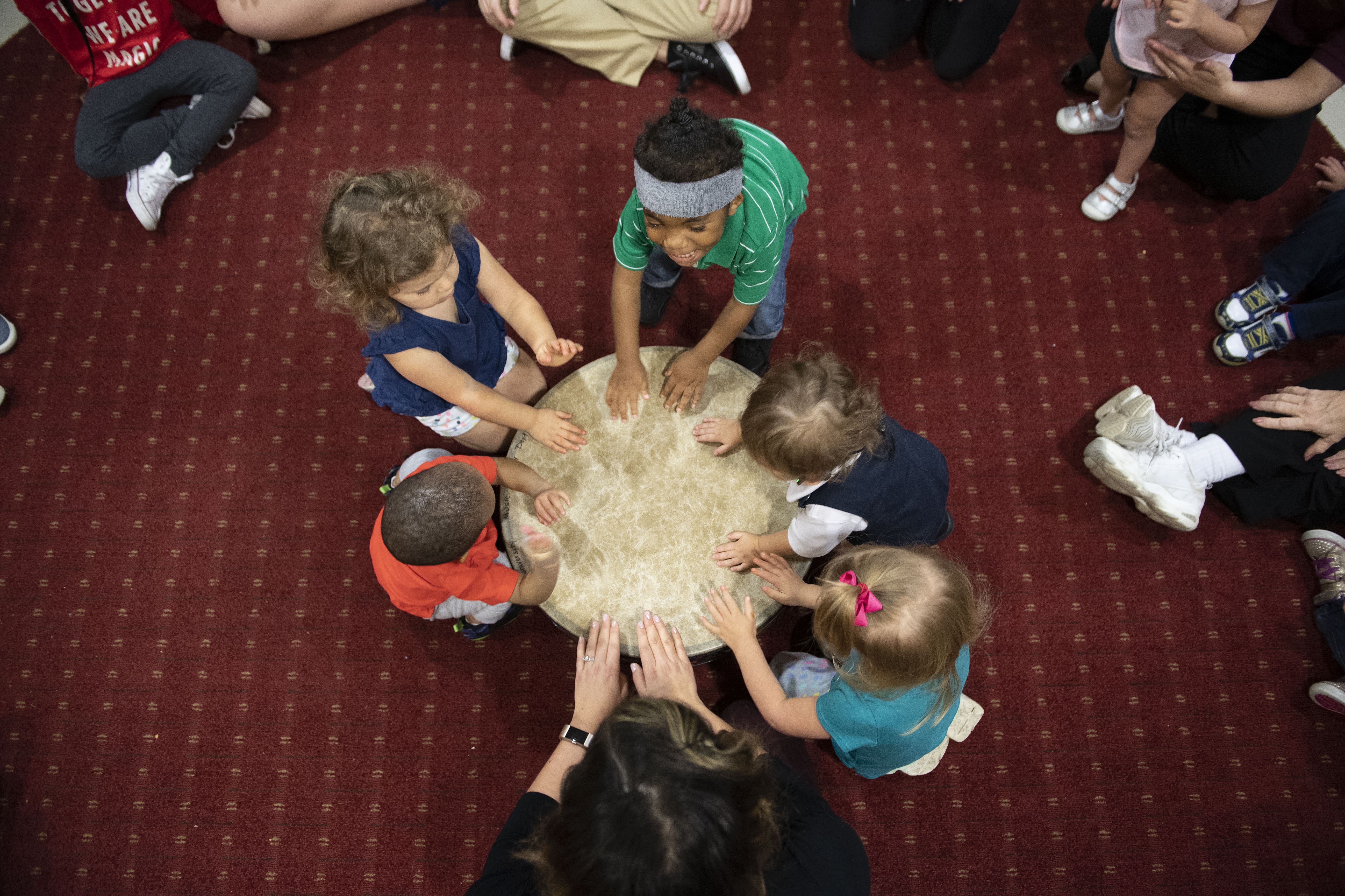 A group of children gather around a large drum, playing it together in a Music Therapy setting.