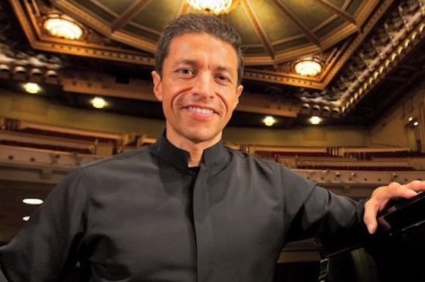 Gustavo Romero posing in an theatre next to a grand piano