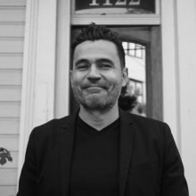 A black and white photo of Dr. Pablo Zavala. He is wearing all black and smiling.