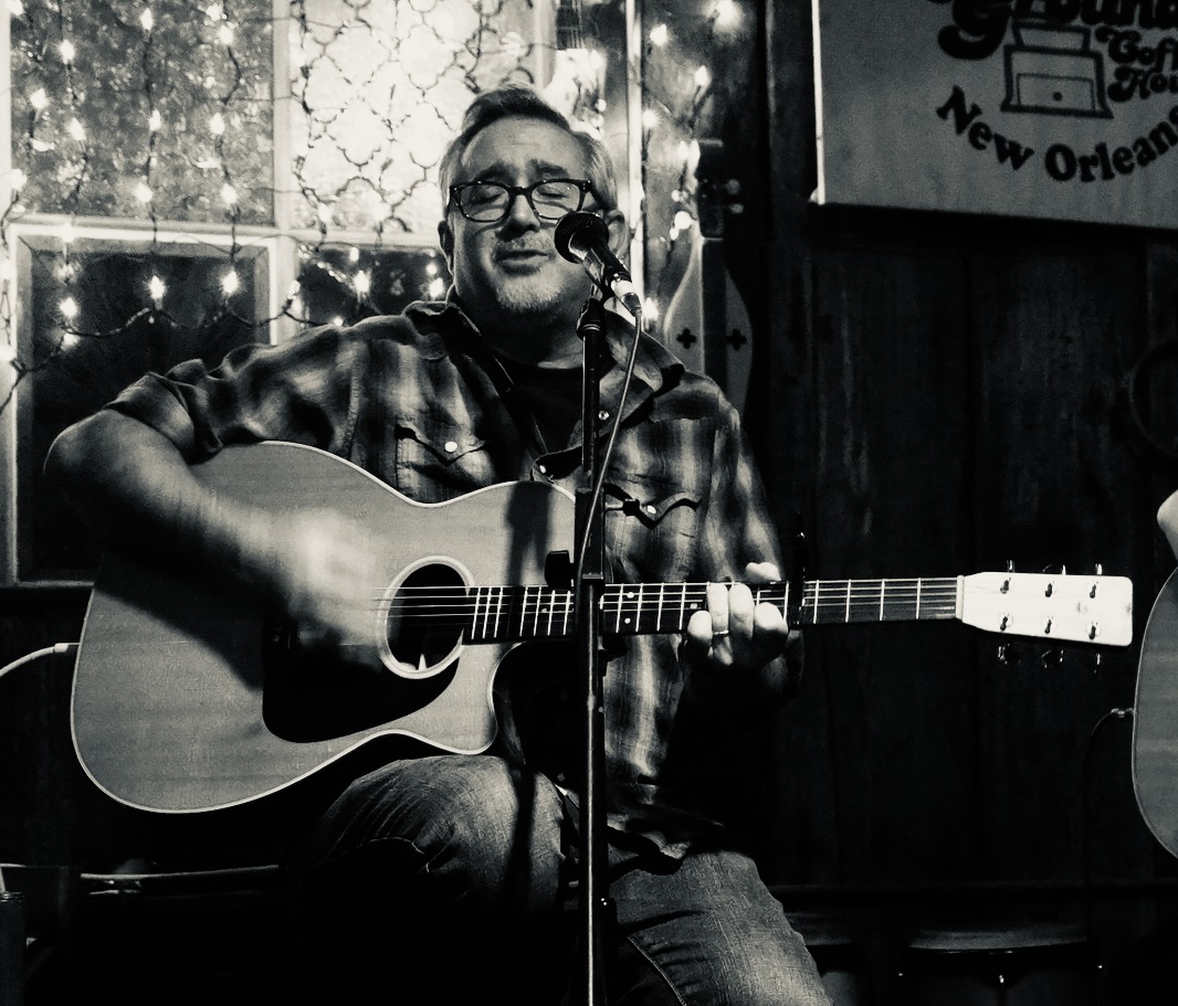 Dr. Mark Fernandez playing a guitar and singing at the old Neutral Ground Bar and Grill