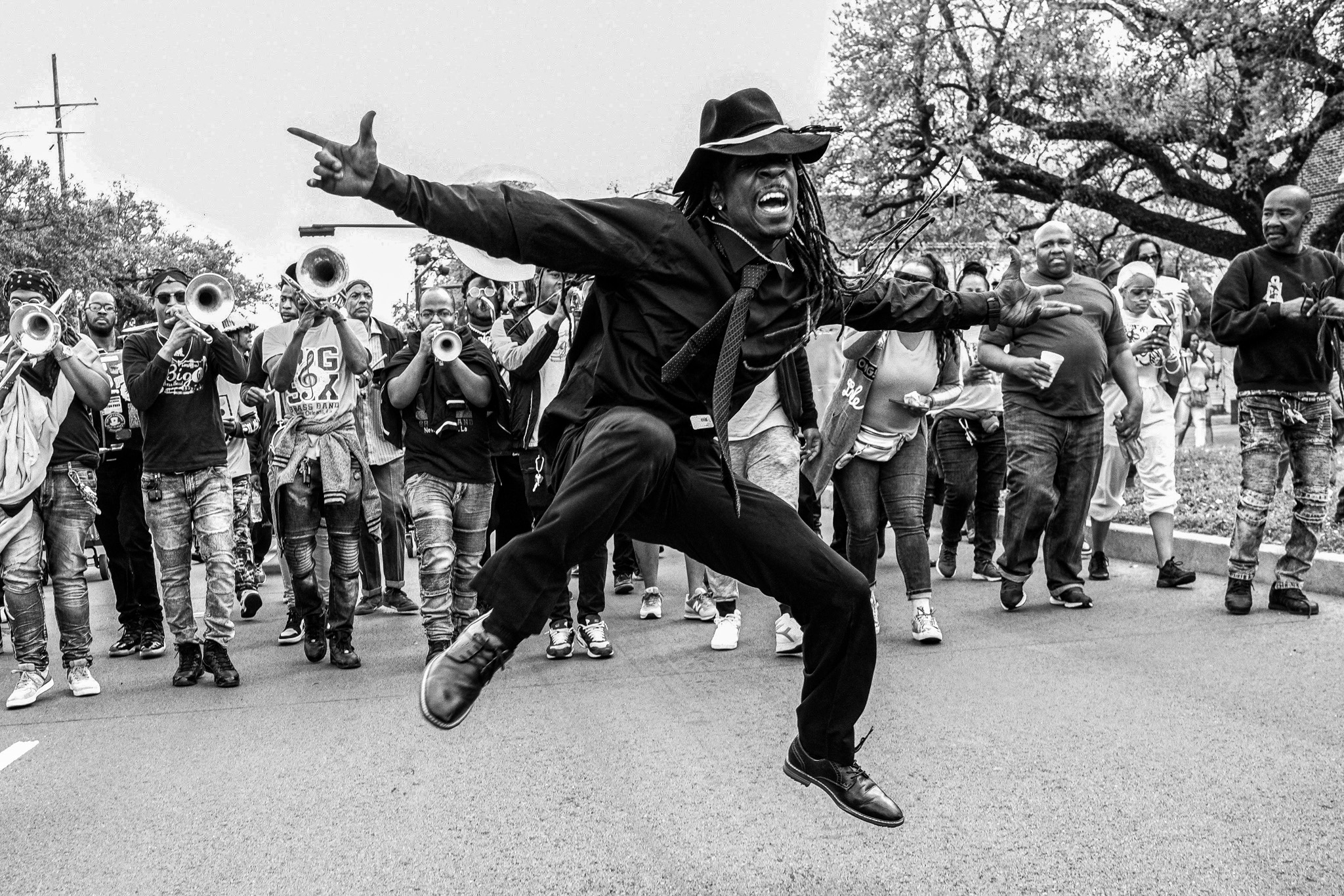 An image of a dancing man leaping into the air while a band of people and musicians follow him